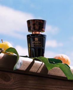 Schwarzer Flakon Olfazeta by Chogan Millésime N°150 auf einem Holzbalken, Apfel und Mandarine unter blauem Himmel